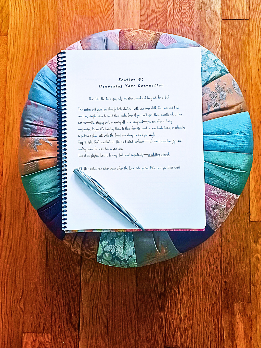 Colorful fabric-covered stool with an open guided journal page to help reparent your inner child beside a pen on a wooden floor