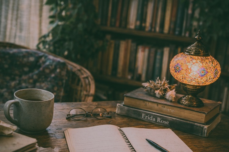 Cozy writing desk with open notebook, half-empty tea mug, Turkish mosaic lamp, and stacked books with the author name Frida Rose on the spine, set in a warm reading nook with a softly blurred bookshelf and greenery.