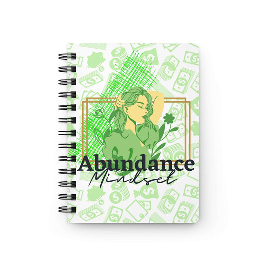 A green spiral notebook with the product name "Abundance Mindset Journal with Journal Prompts" on it, featuring journal prompts.