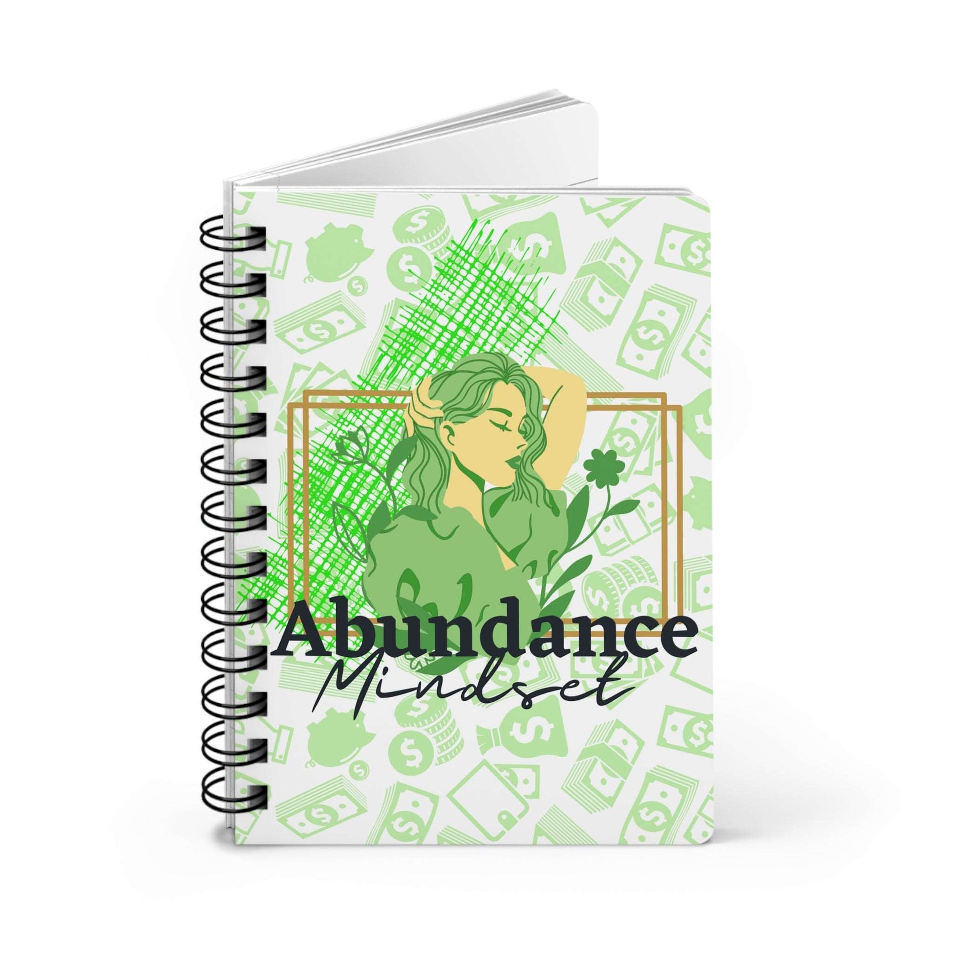 A spiral notebook with the words Abundance Mindset Journal with Journal Prompts on it.