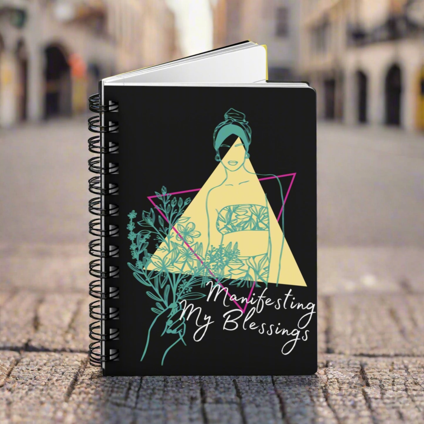 An "Manifesting My Blessings" Daily Affirmation Journal with the words "Meditate my blessings" on a black spiral notebook.