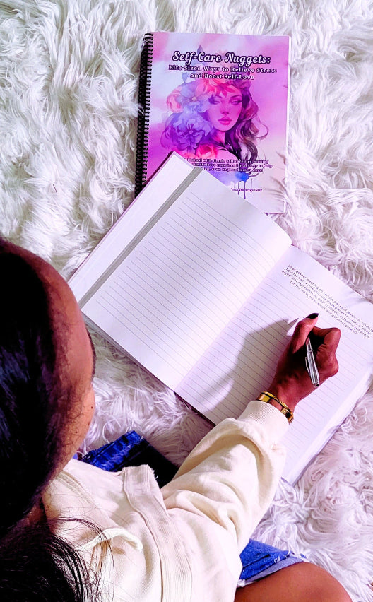 Person writing in a notebook with a purple book titled 'Self-Care Nuggets' on a fluffy white surface.