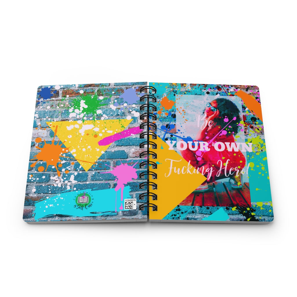 A "Be Your Own Fucking Hero" Spiral Bound Journal for Black Women with colorful splatters on it, perfect for self-reflection and new beginnings.